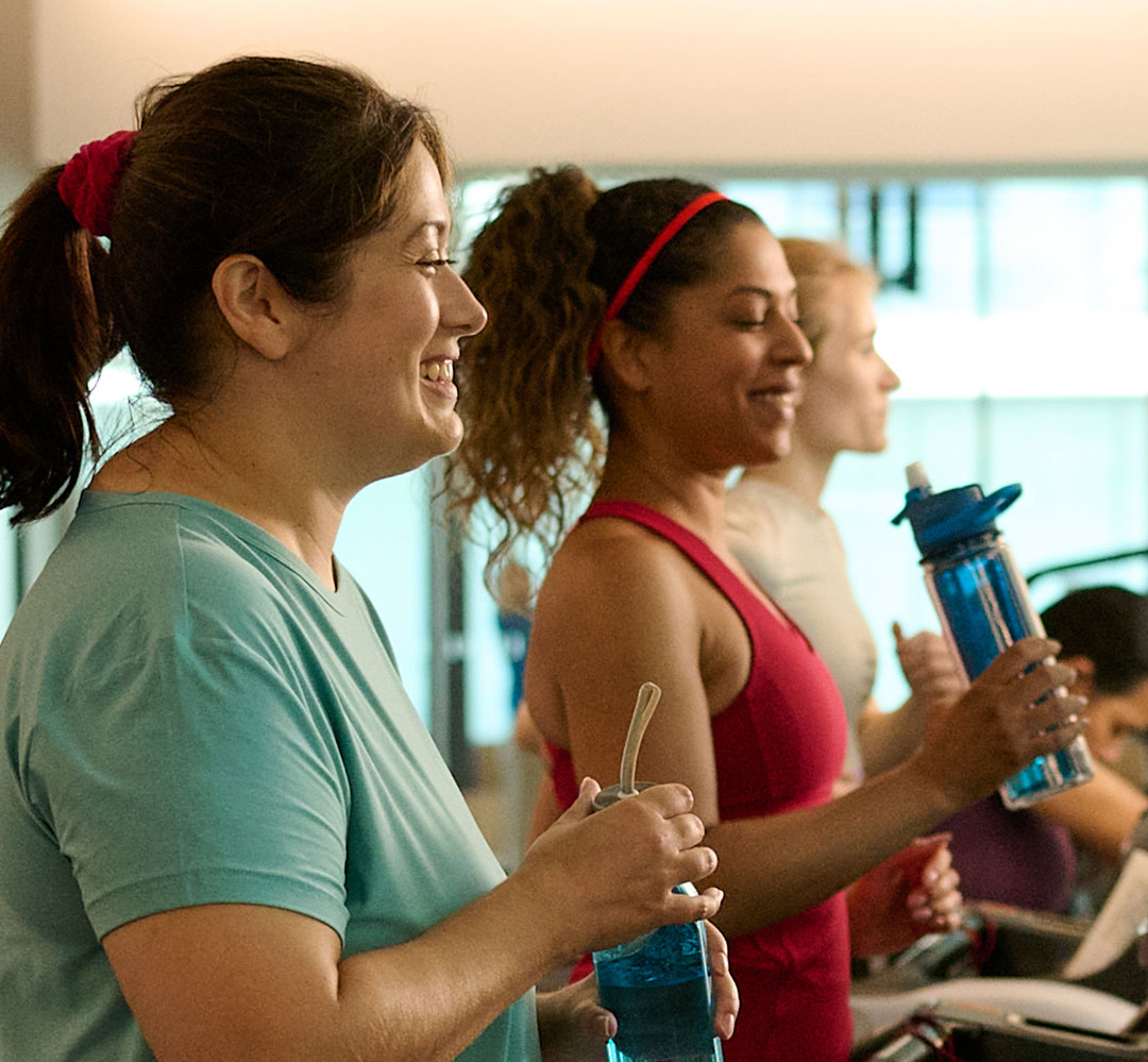 two women chatting and laughing while walking on treadmills