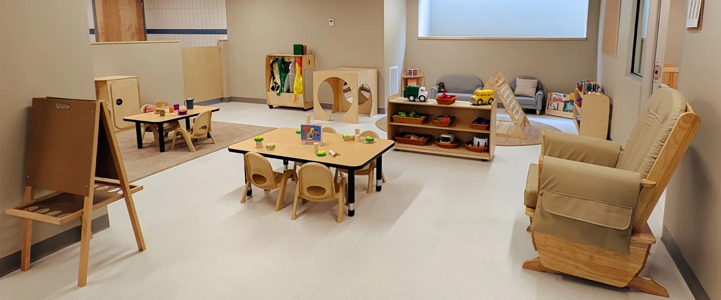 child care room with tables, toys, books, and comfy chairs