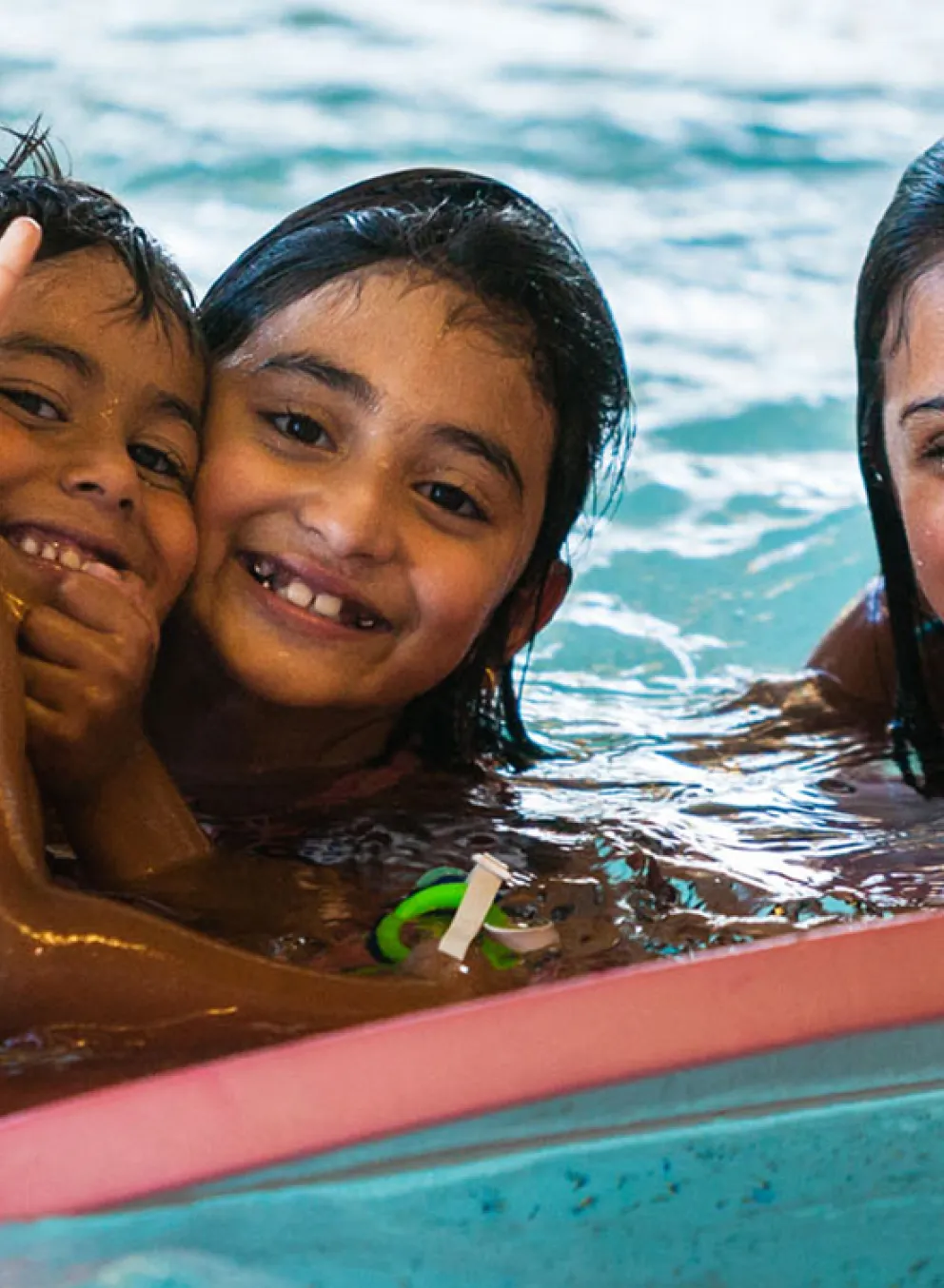 Three kids smiling in the pool