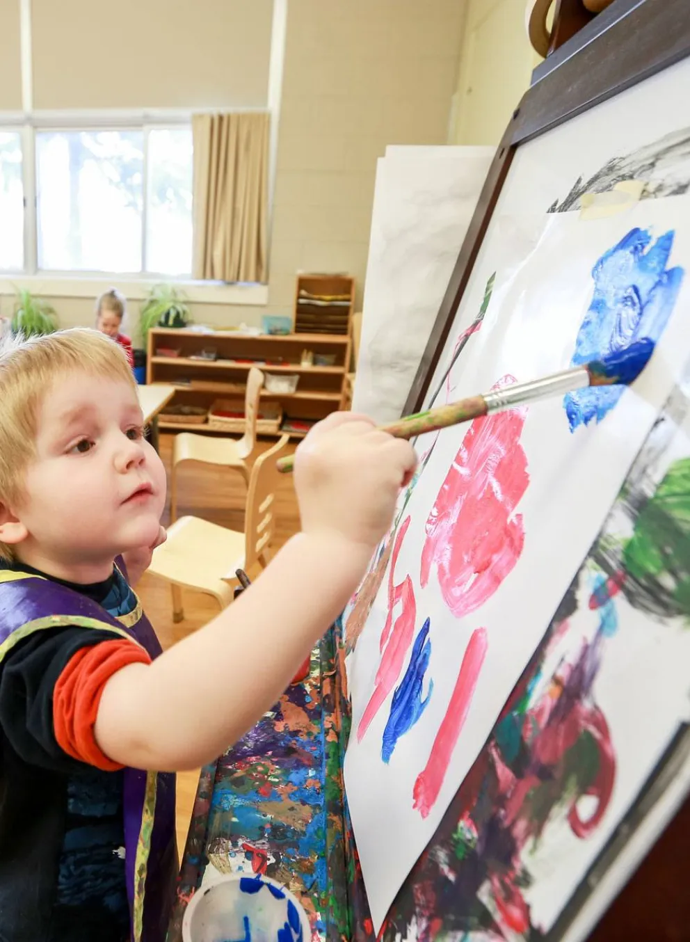 Child painting with brush and easel