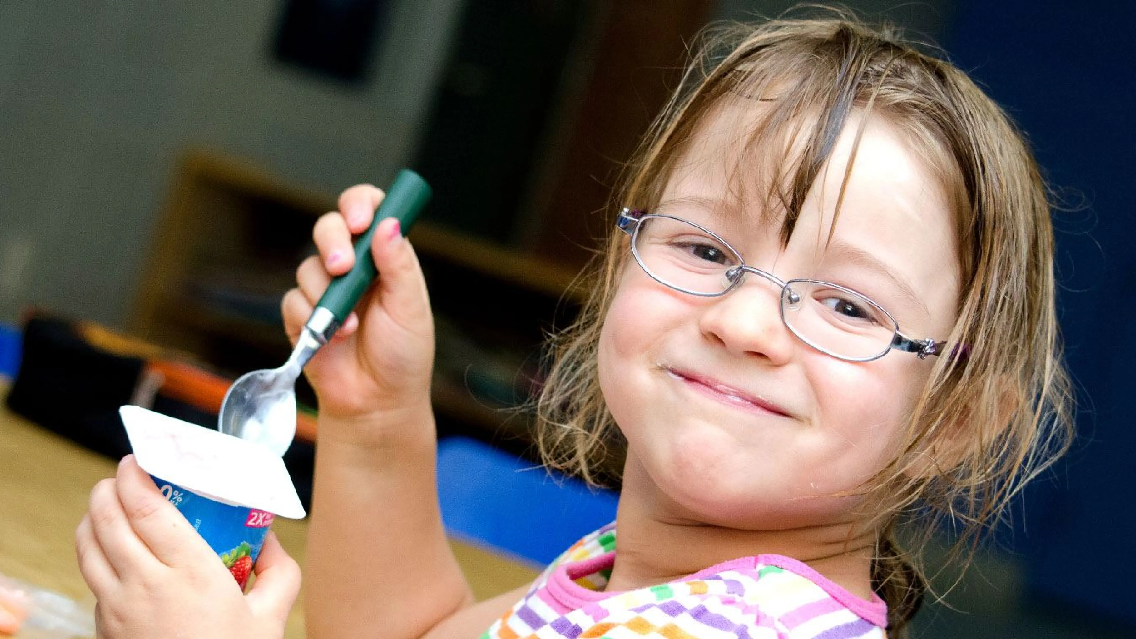 child with glasses eats yogurt and carrots