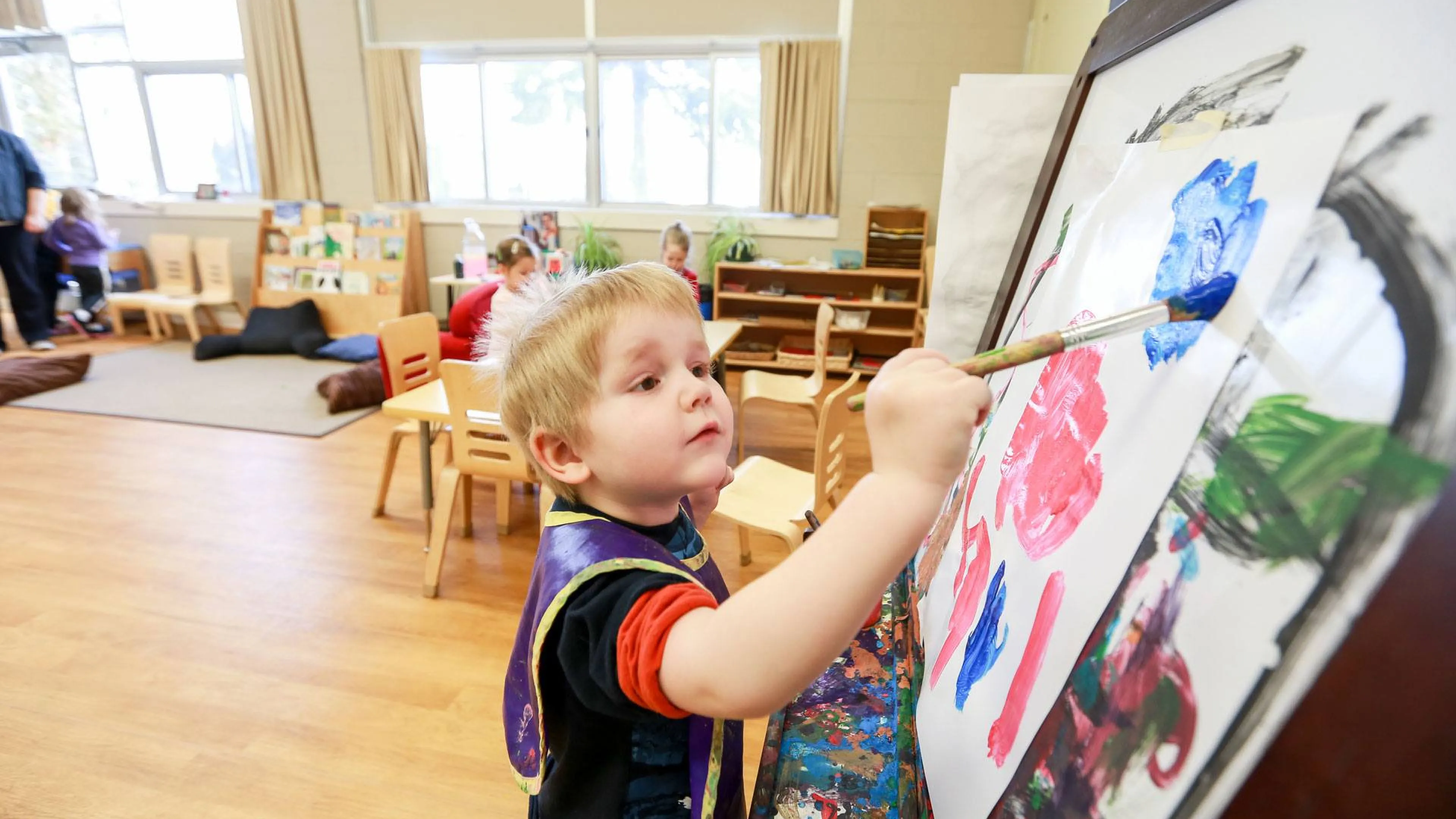Child painting with brush and easel