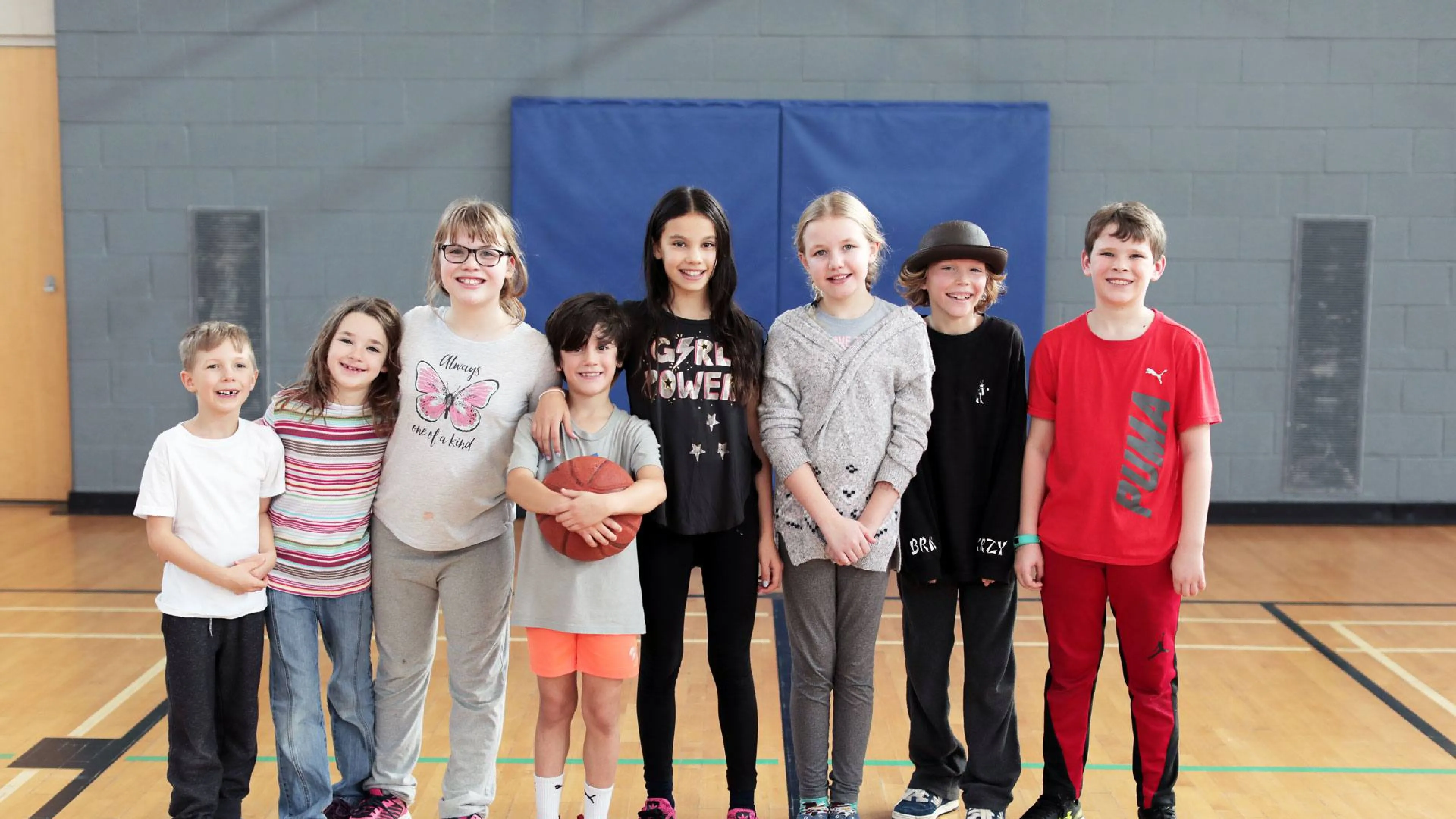 8 smiling kids of different ages standing in gymnasium together