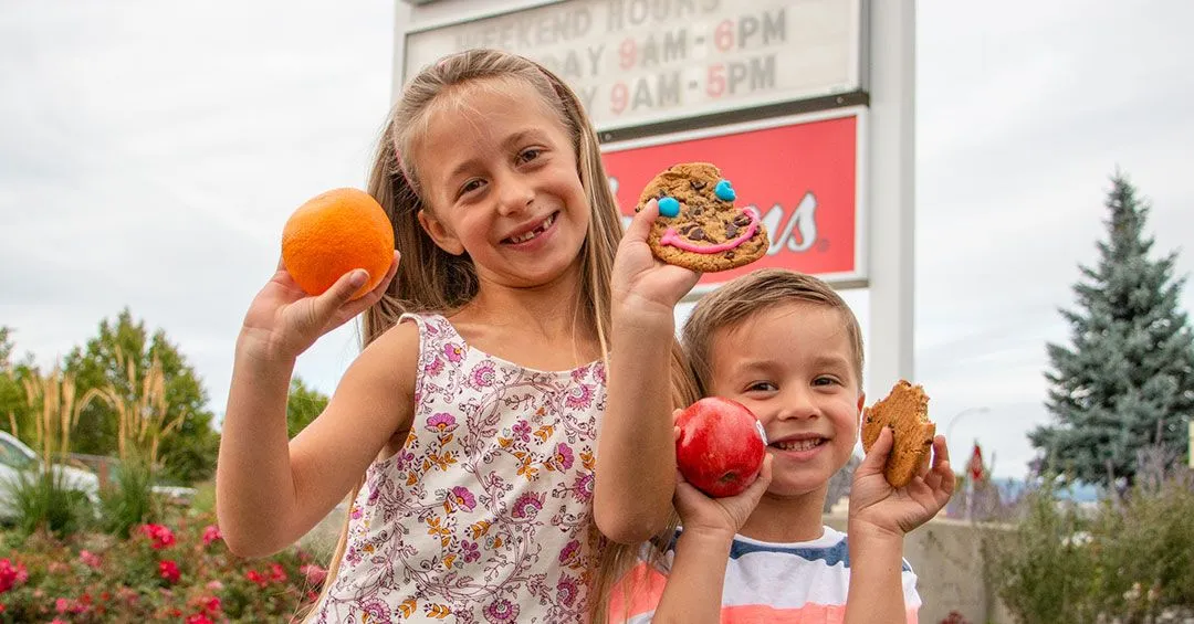 kids holding fruit and Smile Cookies in front of Tim Hortons sign