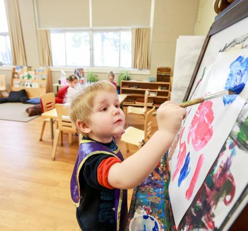 Child painting with brush and easel